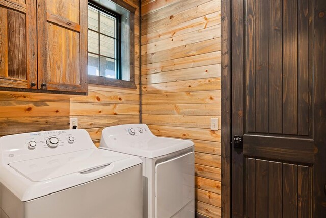 laundry room with wood walls, washer and clothes dryer, and cabinets