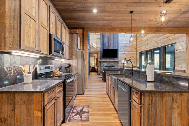 kitchen featuring wood walls, stainless steel appliances, hanging light fixtures, and light hardwood / wood-style flooring