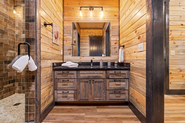 bathroom featuring hardwood / wood-style floors, vanity, a tile shower, and wooden walls