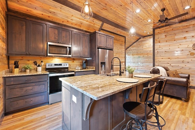 kitchen with lofted ceiling, light hardwood / wood-style flooring, an island with sink, appliances with stainless steel finishes, and light stone counters