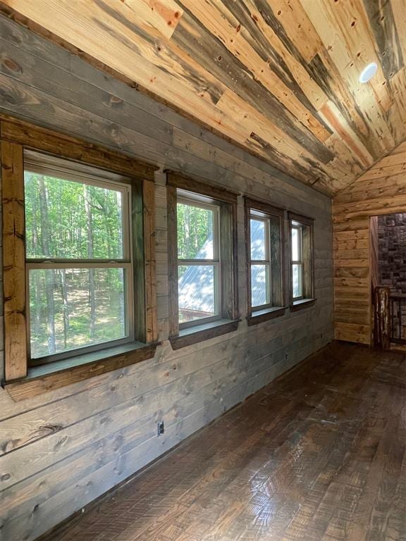 unfurnished room with dark hardwood / wood-style floors, vaulted ceiling, a wealth of natural light, and wooden walls