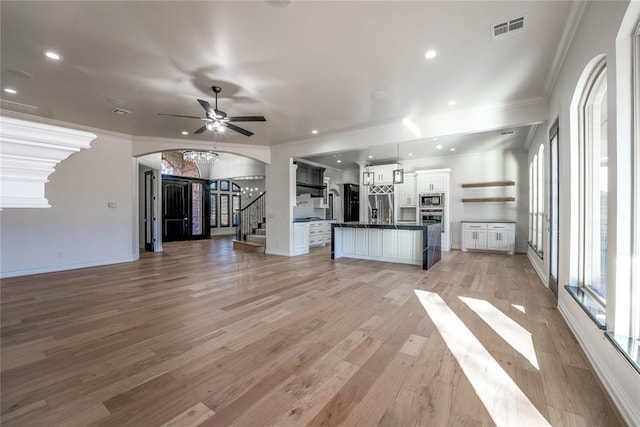 5900 N Choctaw Rd, Choctaw, OK 73020 - unfurnished living room featuring arched walkways, ornamental molding, stairs, light wood-style flooring, and ceiling fan