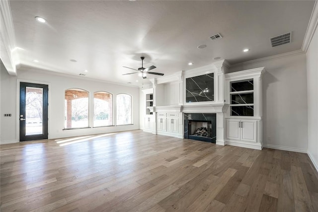 unfurnished living room featuring built in shelves, ceiling fan, a high end fireplace, crown molding, and hardwood / wood-style flooring