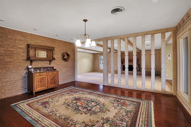 unfurnished dining area featuring dark wood-type flooring, brick wall, and an inviting chandelier