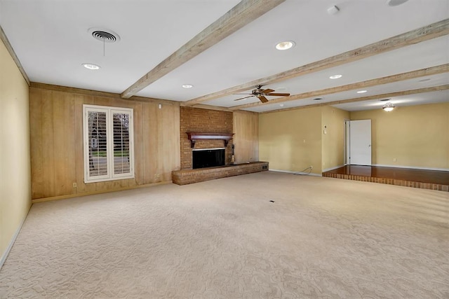 unfurnished living room featuring ceiling fan, a brick fireplace, beamed ceiling, wood walls, and carpet floors