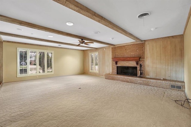 unfurnished living room featuring light carpet, wooden walls, ceiling fan, a fireplace, and beam ceiling