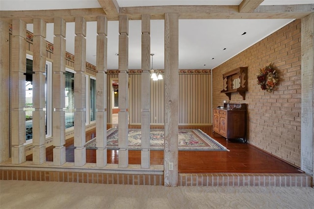 interior space with wood-type flooring, beam ceiling, a notable chandelier, and brick wall