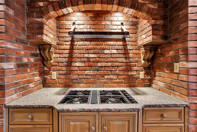 kitchen with stone countertops, stainless steel gas stovetop, and brick wall