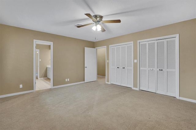 unfurnished bedroom featuring light carpet, connected bathroom, ceiling fan, and multiple closets