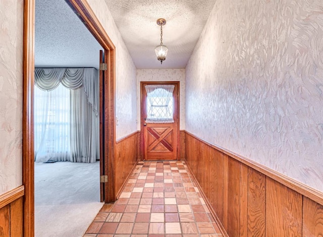 doorway to outside featuring light carpet, a textured ceiling, and wood walls