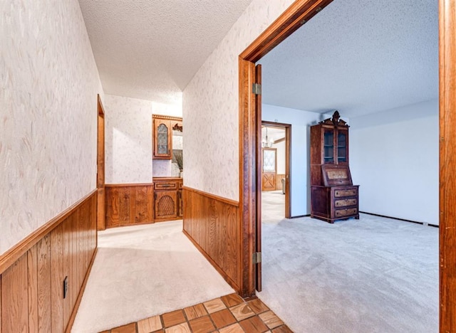 corridor featuring wood walls, light colored carpet, and a textured ceiling