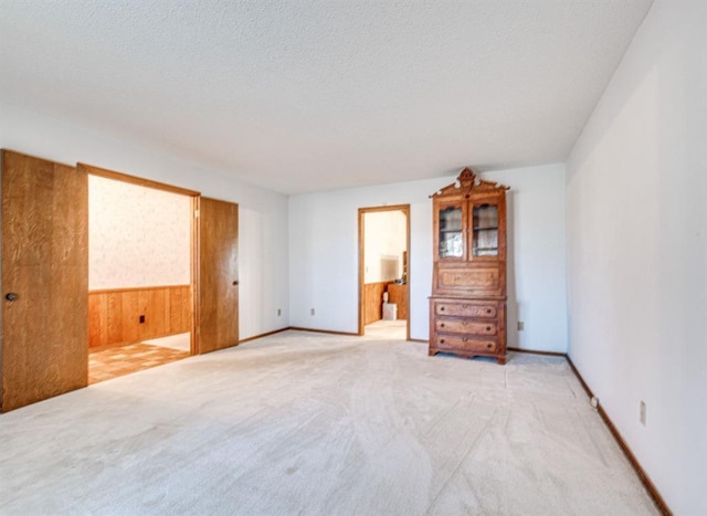 unfurnished room featuring light carpet, a textured ceiling, and wood walls