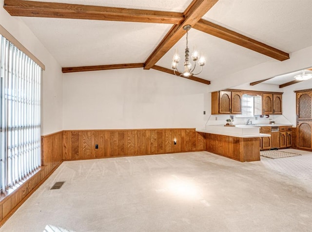 kitchen with lofted ceiling with beams, kitchen peninsula, wood walls, pendant lighting, and light carpet