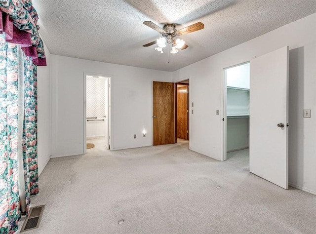 unfurnished bedroom featuring a textured ceiling, light colored carpet, a spacious closet, and ceiling fan