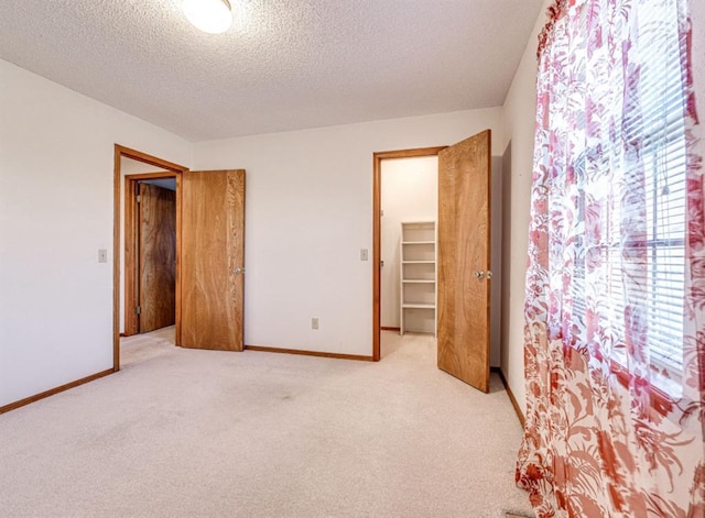 unfurnished bedroom with light carpet, a textured ceiling, a spacious closet, and a closet