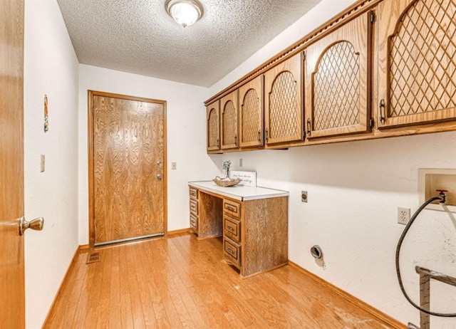 washroom featuring electric dryer hookup, cabinets, washer hookup, a textured ceiling, and light hardwood / wood-style floors