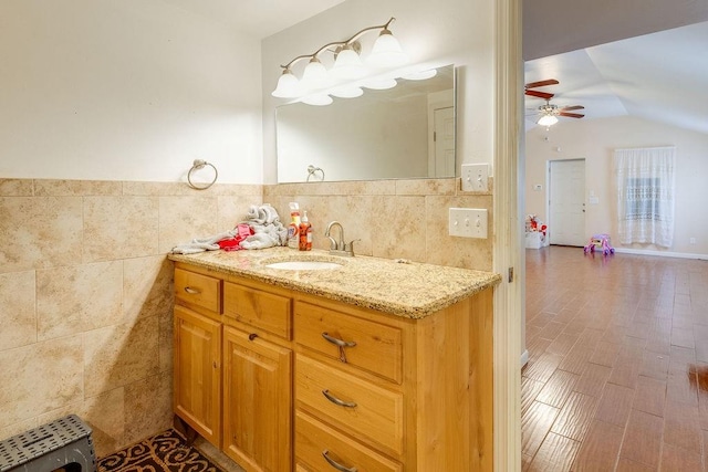 bathroom with ceiling fan, hardwood / wood-style floors, vanity, and tile walls