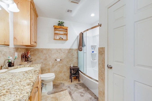 full bathroom with tile patterned flooring, toilet, shower / bath combination with glass door, vanity, and tile walls