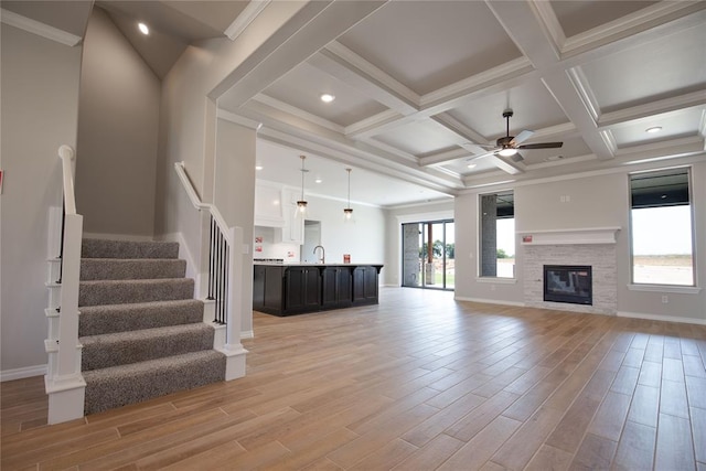 unfurnished living room featuring light wood-type flooring, coffered ceiling, ceiling fan, sink, and beamed ceiling