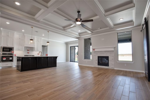 kitchen with light wood-type flooring, black microwave, a center island with sink, white cabinets, and oven