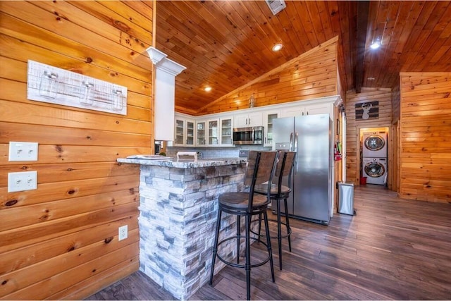 bar featuring appliances with stainless steel finishes, stacked washing maching and dryer, light stone counters, white cabinetry, and wood walls