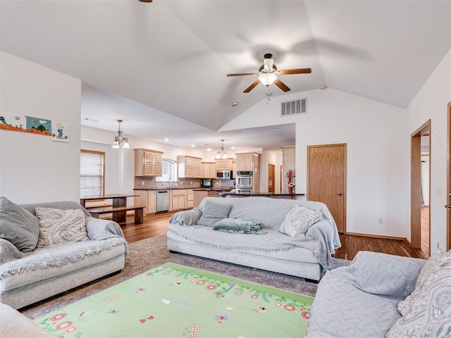 living room featuring ceiling fan with notable chandelier, vaulted ceiling, and light hardwood / wood-style flooring