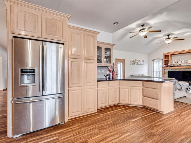 kitchen featuring stainless steel refrigerator with ice dispenser, light wood-type flooring, light brown cabinetry, backsplash, and lofted ceiling