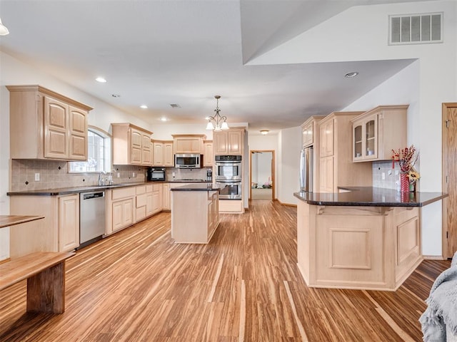 kitchen with an inviting chandelier, tasteful backsplash, kitchen peninsula, appliances with stainless steel finishes, and light wood-type flooring