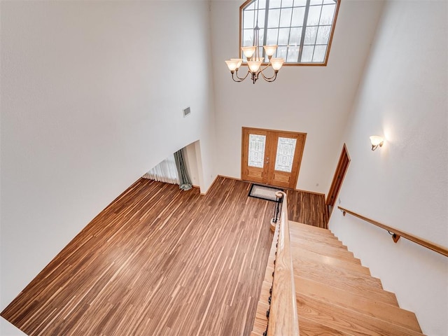 stairs with a high ceiling, an inviting chandelier, french doors, and hardwood / wood-style floors