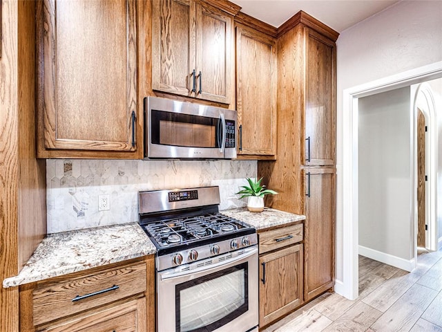 kitchen with appliances with stainless steel finishes, light wood-type flooring, tasteful backsplash, and light stone counters