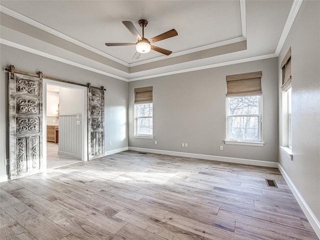 unfurnished room with a raised ceiling, light hardwood / wood-style flooring, ceiling fan, a barn door, and ornamental molding