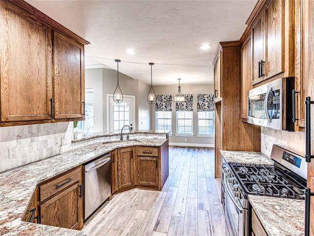 kitchen with sink, light stone countertops, appliances with stainless steel finishes, light hardwood / wood-style floors, and kitchen peninsula