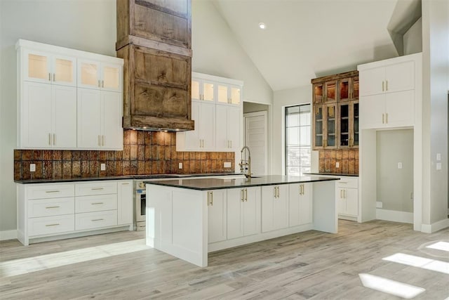 kitchen featuring a center island with sink, white cabinets, light wood-type flooring, and high vaulted ceiling