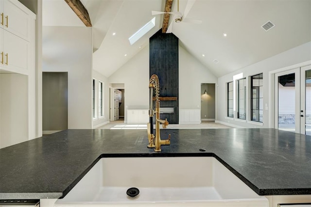 kitchen with high vaulted ceiling, a skylight, ceiling fan, beam ceiling, and white cabinetry