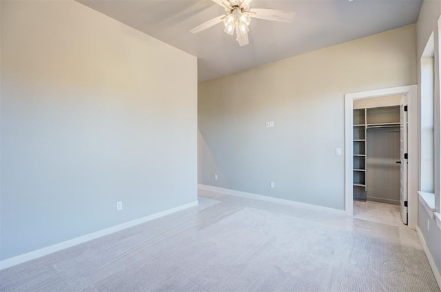 unfurnished bedroom with light carpet, a walk in closet, a closet, and ceiling fan