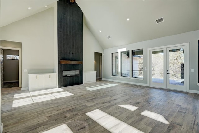 unfurnished living room with a large fireplace, french doors, high vaulted ceiling, and light hardwood / wood-style floors