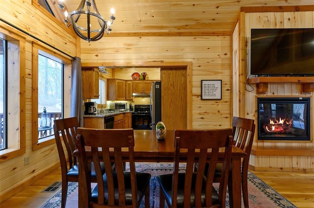 dining room featuring a multi sided fireplace, wood walls, a chandelier, and light wood-type flooring