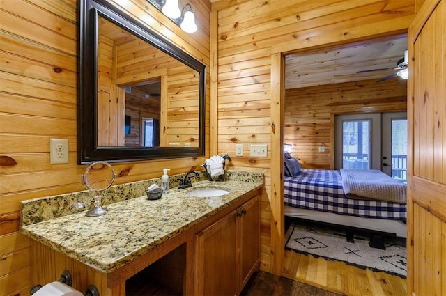 bathroom featuring wood-type flooring, vanity, ceiling fan, and wooden walls