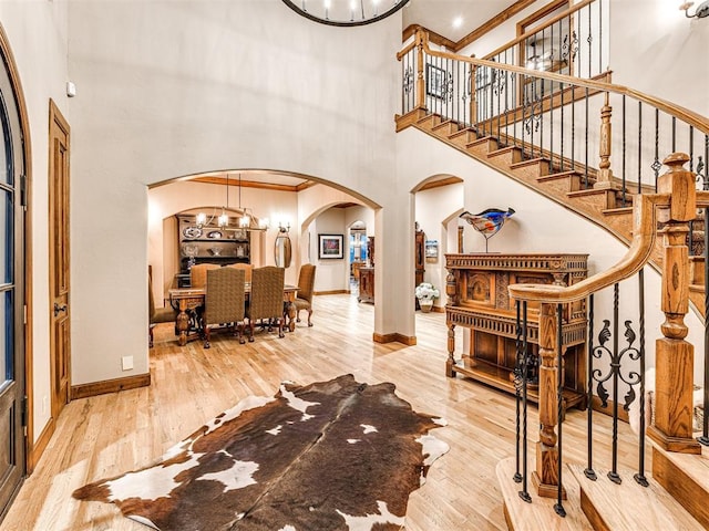 foyer with ornamental molding, a towering ceiling, wood-type flooring, and an inviting chandelier