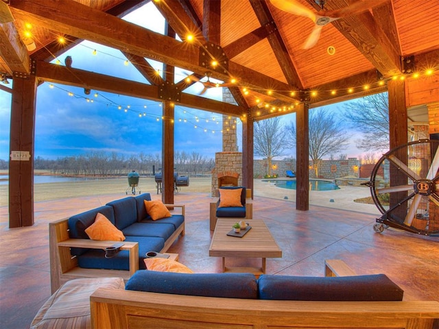 patio terrace at dusk with a gazebo, ceiling fan, a water view, and an outdoor living space with a fireplace