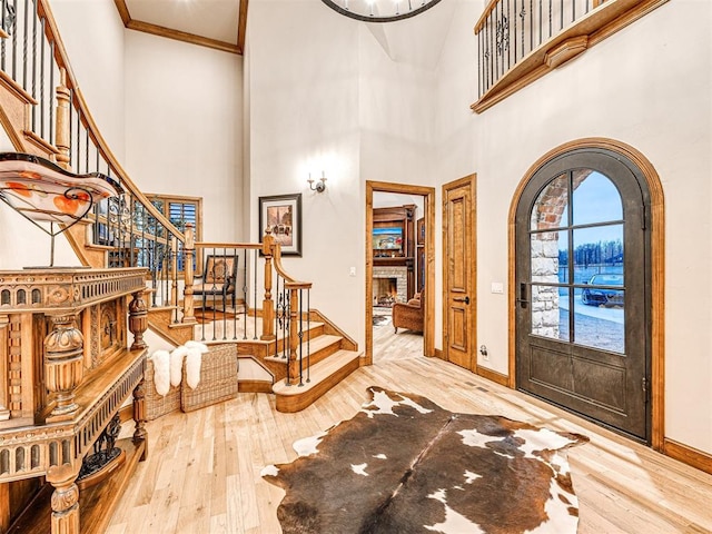 foyer featuring hardwood / wood-style floors, a brick fireplace, crown molding, and a high ceiling