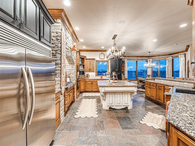 kitchen featuring light stone countertops, a center island, an inviting chandelier, built in fridge, and decorative light fixtures