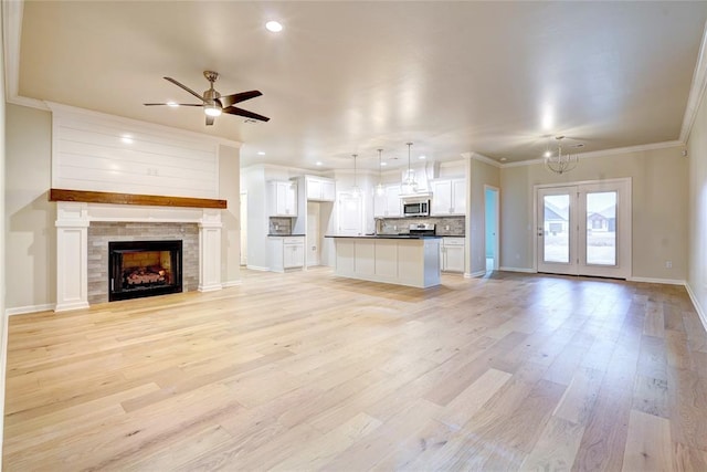 unfurnished living room with ceiling fan with notable chandelier, sink, crown molding, light wood-type flooring, and a tiled fireplace