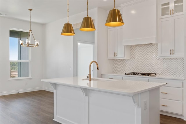 kitchen featuring white cabinetry, a center island with sink, decorative light fixtures, and custom range hood