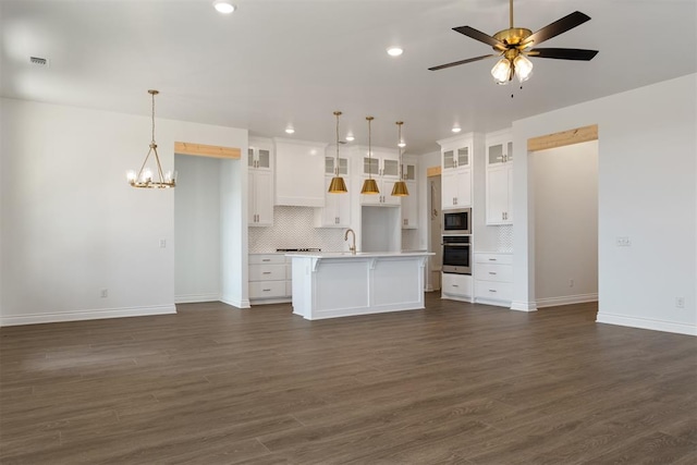 kitchen featuring stainless steel appliances, dark hardwood / wood-style flooring, decorative light fixtures, a center island with sink, and white cabinets