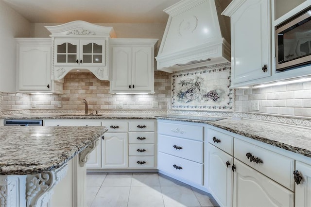 kitchen featuring stainless steel microwave, premium range hood, sink, decorative backsplash, and white cabinetry