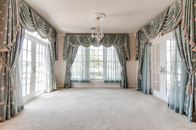 carpeted empty room with an inviting chandelier and french doors