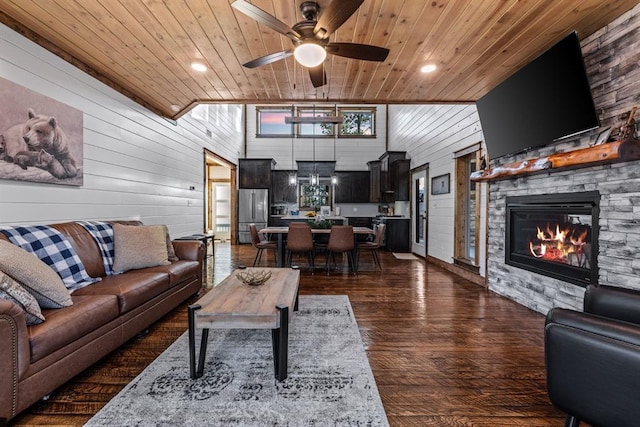 living room with ceiling fan, a stone fireplace, wooden walls, and wooden ceiling