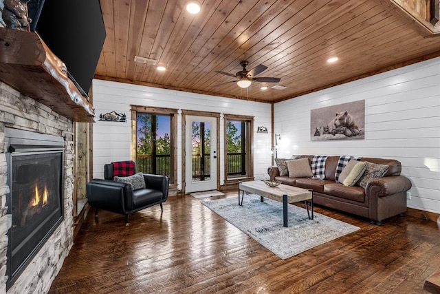 living room with ceiling fan, dark hardwood / wood-style floors, wooden walls, a stone fireplace, and wooden ceiling