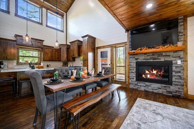 dining room featuring high vaulted ceiling, a stone fireplace, plenty of natural light, dark hardwood / wood-style flooring, and wood ceiling